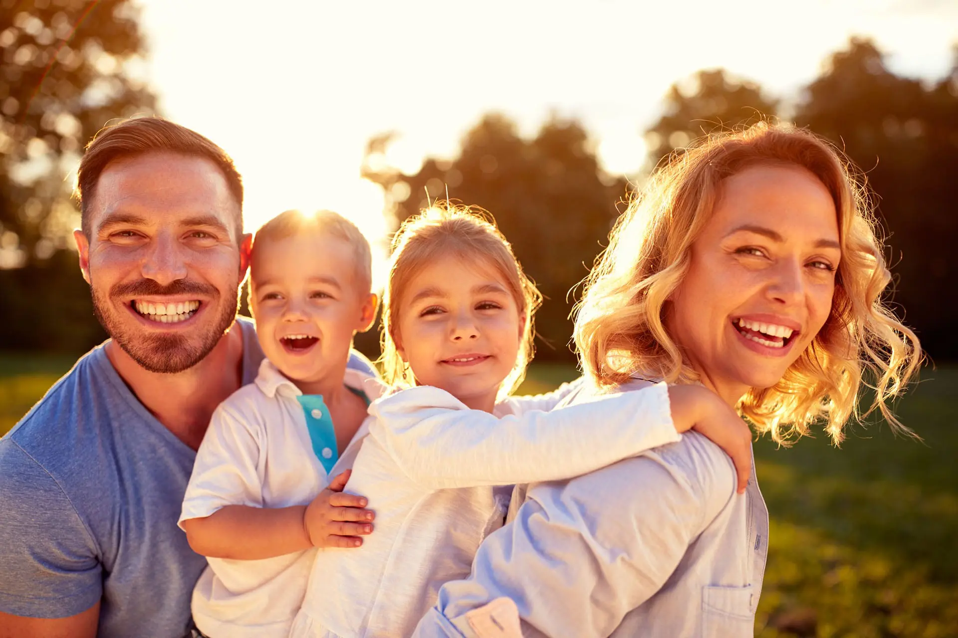A mother and father and their young children smile at the camera, showing their clean healthy teeth.